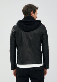 Zwarte leren jas met een getailleerd ontwerp, voorzien van een zwarte capuchon en rode accenten langs de schouders. Gladde textuur en minimale stikseldetails.