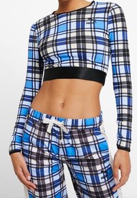 Långärmad cropped topp och joggingbyxor i en rutigt mönster med blått, svart och vitt. Tyget är slätt; midjebandet har ett svart elastiskt band.