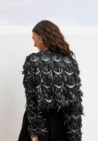 Zwarte cropped jas met ingewikkelde kralenfranje in een ruitpatroon, met een gestructureerd oppervlak en een gelaagd ontwerp.