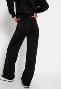 Schwarze Sweatpants mit lockerer Passform, elastischem Bund und weichem Material. Der Stoff ist glatt und wird durch einen leicht ausgestellten Beinbereich ergänzt.