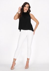 Sort ærmeløs top med høj krave, hvide skinny jeans og guldhæle med remme. Glat stof og afslappet pasform, der giver et moderne look.