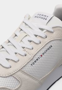 Λευκό και μπεζ αθλητικό παπούτσι Tommy Hilfiger με πάνελ από δίχτυ και σουέτ, λευκά κορδόνια και λογότυπο της μάρκας στη γλώσσα και την πλευρά.