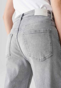 Jeans in denim grigio chiaro con un design a vita alta, due tasche posteriori e una patch in pelle bianca sulla vita.