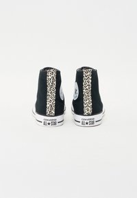 Svart høyhælte joggesko med leopardmønstrede sidepaneler, gummisåler, og Converse All Star-merke på hælen og tungen.