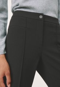 Černé tailored kalhoty s elegantním designem, které mají postranní kapsy a zapínání na knoflík. Tkanina má hladký, matný povrch.