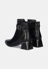 Botas de tobillo de cuero negro con un panel texturizado, acentos de tachuelas y un tacón de bloque metálico. Cierre lateral con cremallera para facilitar el calzado.