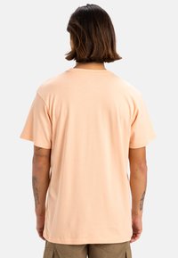 Camiseta de algodón color melocotón con cuello redondo, mangas cortas y un corte relajado, mostrada desde la parte de atrás. Diseño minimalista, textura suave.