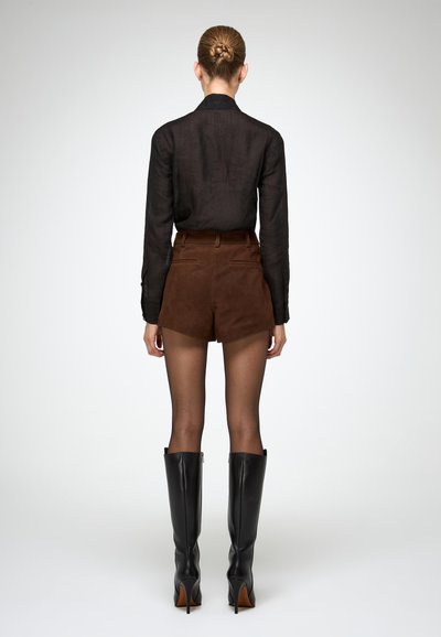 Cămașă neagră cu mâneci lungi, pantaloni scurți din suede maro cu talie înaltă și cizme negre din piele cu toc stiletto până la genunchi. Textură netedă și design simplu.