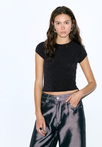 Tricou negru scurt cu mâneci scurte, împodobit cu mici puncte argintii. Asortat cu blugi închiși la culoare, lucioși, și accesorii argintii.