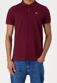 Burgundy polo shirt with a classic collar, short sleeves, and a small logo on the chest, made of a smooth, breathable fabric.