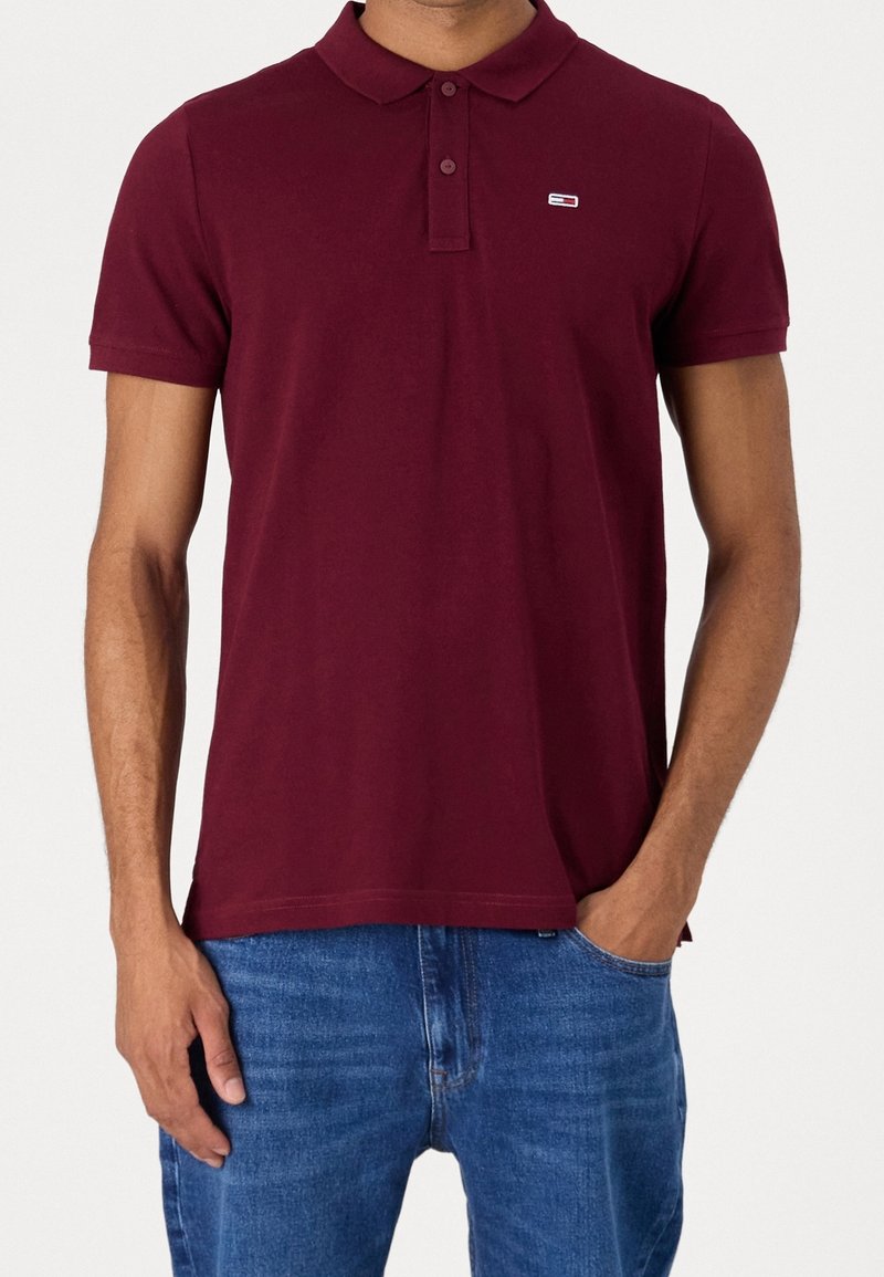 Burgundy polo shirt with a classic collar, short sleeves, and a small logo on the chest, made of a smooth, breathable fabric.