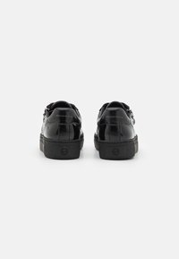 Sneaker in pelle patent nera con forma arrotondata, suola in gomma testurizzata e dettagli in argento. Logo impresso sul tallone, design minimalista.