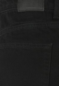 Tissu en denim noir avec une texture lisse, un détail de patch à la taille, et des coutures discrètes le long des poches et des coutures.