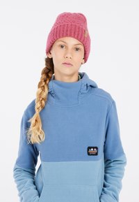 Sweat à capuche en polaire bleu clair avec une section inférieure bleu foncé et un petit patch logo. Béret en tricot rose avec un motif texturé sur le dessus.