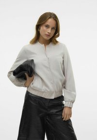 Ljusgrå bomberjacka med rund halsringning, framknäppning och elastiska ärmslut, kombinerad med svarta strukturerade läderbyxor.