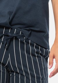 Navyblauw katoenen t-shirt met een losse pasvorm, gecombineerd met navy gestreepte broek met trekkoord en witte verticale strepen en een strik aan de voorkant.
