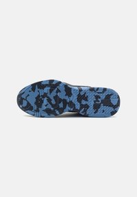 Semelle de chaussure avec motif camouflage noir et bleu et bande de roulement texturée pour l’adhérence, présentée sur un fond clair uni.