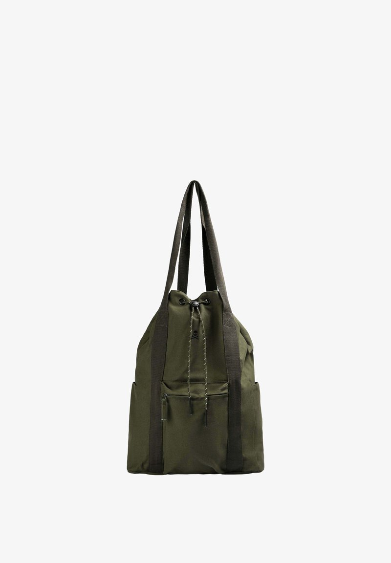 Grøn stofrygsæk med sorte webbed remme, med snørelukning og forlommek; minimalistisk design, blød tekstur.