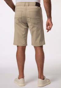 Pantaloni corti in cotone beige con un taglio dritto, dotati di tasche posteriori e una texture liscia. Indossati con sneakers di colore chiaro.