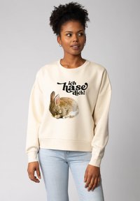 Sweatshirt de couleur crème avec des manches longues, présentant un lapin qui dort imprimé et le texte "ich hase dich !" en noir gras. Texture de tissu douce.