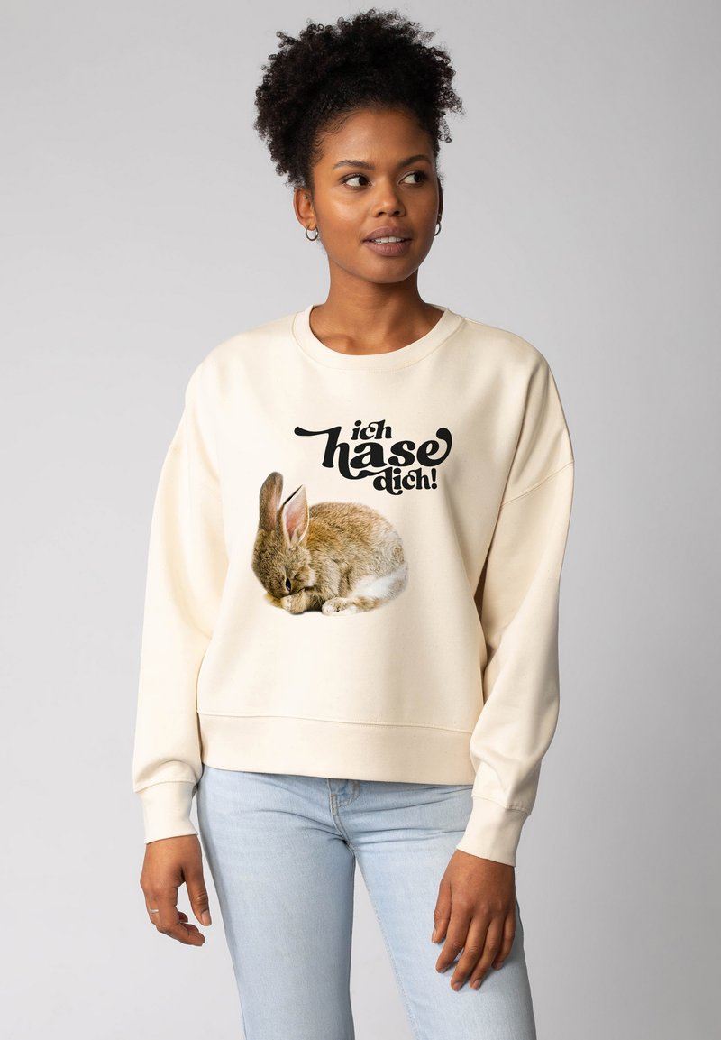 Sweatshirt de couleur crème avec des manches longues, présentant un lapin qui dort imprimé et le texte "ich hase dich !" en noir gras. Texture de tissu douce.