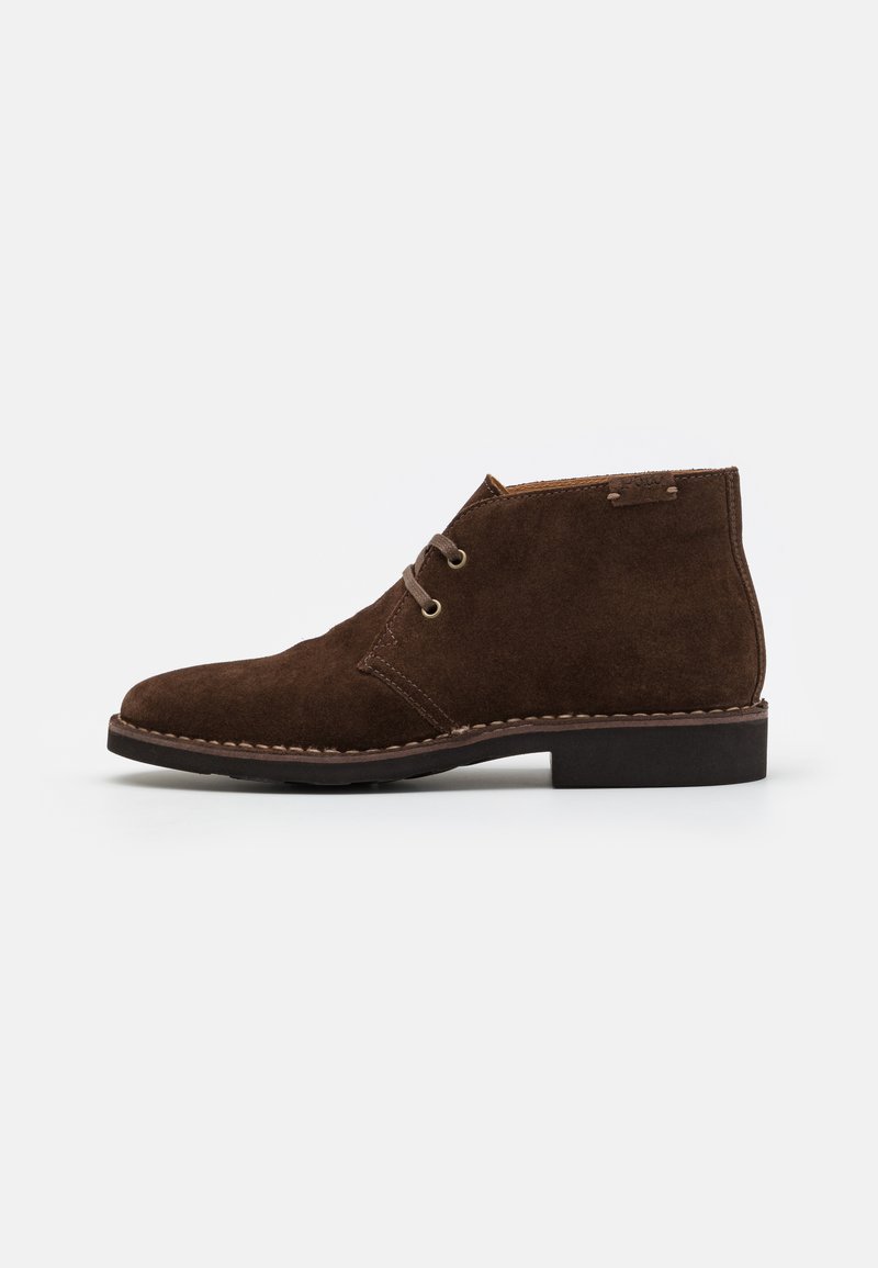 Botas de tobillo de ante marrón con puntera redondeada, detalles de costura, cierre con cordones y un tacón bajo de goma. Diseño simple y clásico.