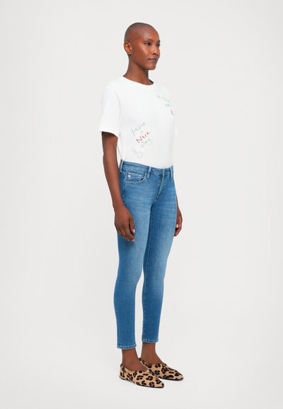 Vit kortärmad t-shirt med färgglad text och grafik, kombinerad med blå skinny jeans och ballerinas i leopardmönster. En enkel, avslappnad outfit.