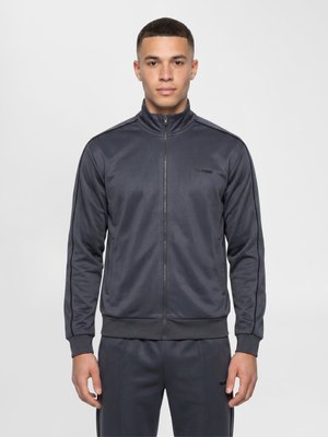 Young man standing facing forward wearing a dark gray zip-up track jacket and matching pants against a plain light background.