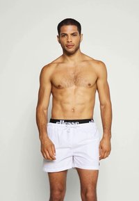 Weiße Badeshorts mit einem schwarzen elastischen Bund, der die Marke "ellesse" trägt. Entworfen mit einer lockeren Passform und einem Kordelzug.