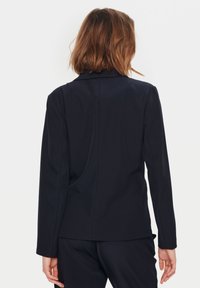 Jūras flotes bleizeris, izgatavots no gludas auduma, ar pielāgotu piegriezumu, garām piedurknēm un vienu atveri aizmugurē. Minimalistisks dizains bez rotājumiem.