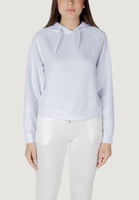 Felpa blu chiaro in morbido tessuto con cappuccio e lacci, caratterizzata da un logo ricamato discreto. Abbinata a leggins bianchi.