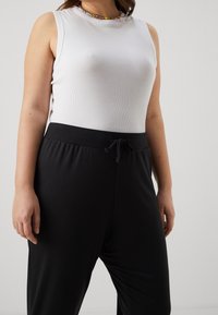 Biały top bez rękawów z prążkowaną fakturą, zestawiony z czarnymi spodniami ze ściągaczem. Gładka tkanina, luźny krój, minimalistyczny design, brak widocznych wzorów.