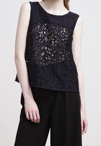 Navy lace top with sleeveless design, featuring floral pattern and sheer sections. Paired with high-waisted black trousers.