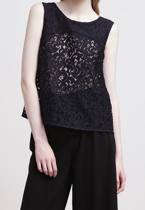 Top in pizzo blu navy con design senza maniche, caratterizzato da un motivo floreale e sezioni trasparenti. Abbinato a pantaloni neri a vita alta.