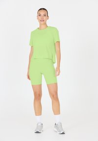 Vihreä urheiluasu, joka koostuu löysästä lyhythihaisesta paidasta ja tiukoista pyöräilyshortseista. Sujuva pinta ja minimalismi.