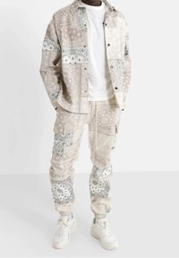 Set di giacca e pantaloni chiari e patterned con design in stile bandana in beige e bianco; vestibilità rilassata con polsi elasticizzati.