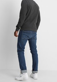 Tmavě šedá mikina s žebrovanými manžetami, doplněná modrými džínami stočenými u kotníků. Bílé tenisky dokončují outfit.