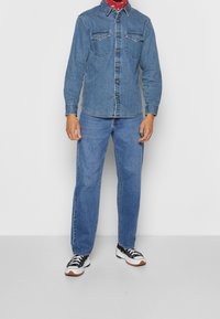 Chemise en denim à manches longues, avec deux poches poitrine et un col boutonné. Associée à un jean bleu clair et des baskets noires et blanches.