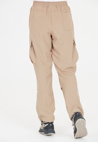 Beige cargobroek met een elastische tailleband, zijzakken en taps toelopende pijpen. Gecombineerd met zwart-grijze wandelschoenen. Gladde stoftextuur.