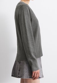 Harmaa neulepusero pitkillä hihoilla, ribbaatut hihansuut ja helma, yhdistettynä farkkuhameeseen. Tekstuuri vaikuttaa pehmeältä ja lämpimältä.