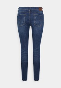 Jeans ajustados en denim azul oscuro con una textura suave, que cuentan con dos bolsillos traseros, costuras en contraste y un parche de cuero en la cinturilla.