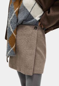 Wikkelrok van imitatieleren bont in lichtbruin met een knoopsluiting, gecombineerd met een grijze gebreide trui met patroon en grijze geribde panty's.