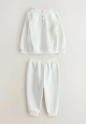 Biely dvojdielny outfit pozostávajúci z dlhého rukáva s čipkovým lemom a tromi gombíkmi, doplnený o nohavice s elastickým pásom v rovnakom prevedení.