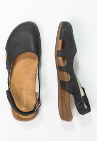 Sandales en cuir noir avec un design ouvert et des accents découpés. Semelles en liège texturé et une sangle arrière pour un soutien. Intérieur doux et moelleux.