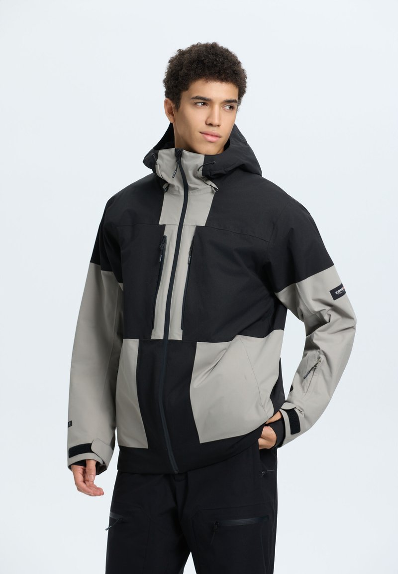 Giacca da uomo in nero e grigio chiaro. Presenta un cappuccio, tasche con zip e un mix di tessuti con finitura testurizzata. Inclusi polsini regolabili.