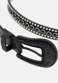 Cinturón de cuero negro con tachuelas plateadas y piedras preciosas redondas, que presenta una hebilla decorativa con relieve y un detalle de correa texturizada.