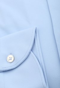 Lichtblauwe textuurstof met een opgevouwen kraag, voorzien van een witte knop en contrasterende stiksels.