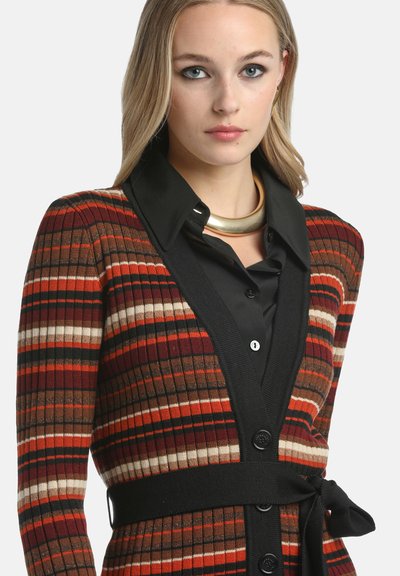 Cardigan cu prindere cu rigle multicolore, cu dungi orizontale în roșu, maroniu și crem. Prezentă accente negre, un brâu și închidere cu nasturi.