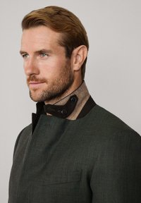 Zelená textúrovaná bunda s vysokým golierom, s hnedým a béžovým akcentom, zapínanie na dvojité gombíky a štíhly, moderný dizajn.