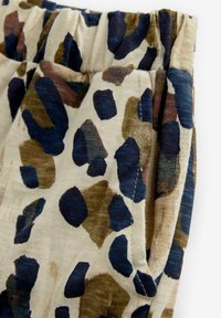 Baumwollhose mit einem cremfarbenen Hintergrund, versehen mit abstrakten blauen, braunen und beigen Flecken. Elastischer Bund mit Falten und sichtbaren Nähdetails.